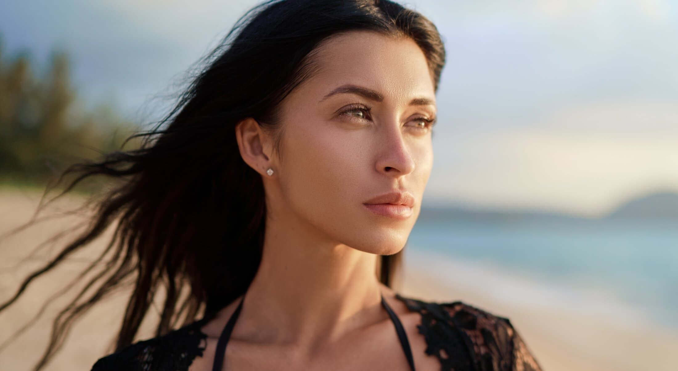 Woman with flowing hair gazing at beach horizon.